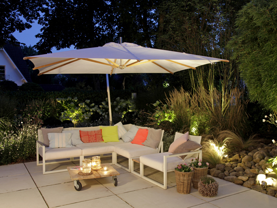 Loungesitzecke auf Gartenterrasse mit weißem Sonnenschirm und Gartenbeleuchtung